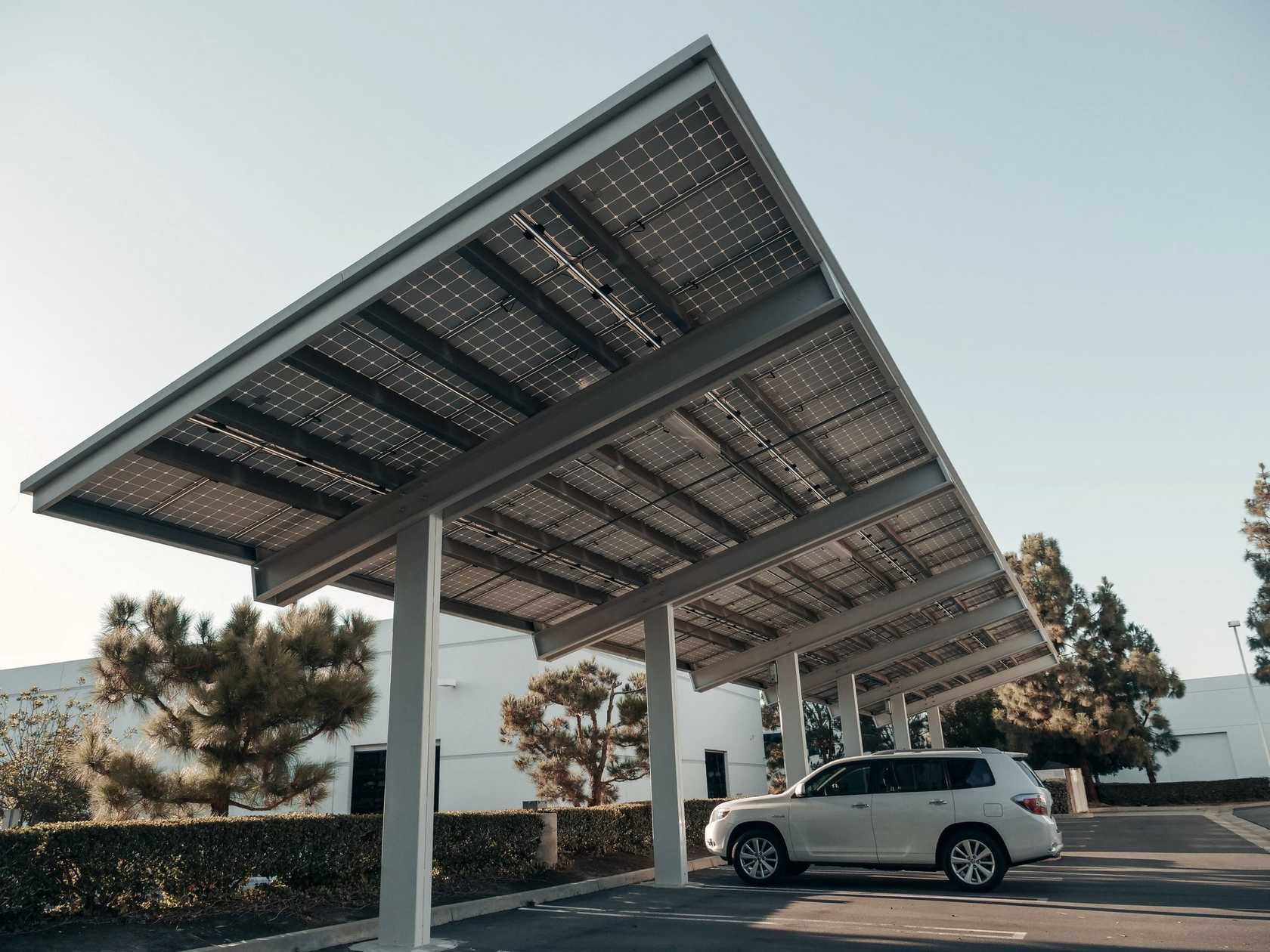 Carport solaire en acier vu en contre-plongée, panneaux photovoltaïques sur fond de ciel clair et voiture garée dessous