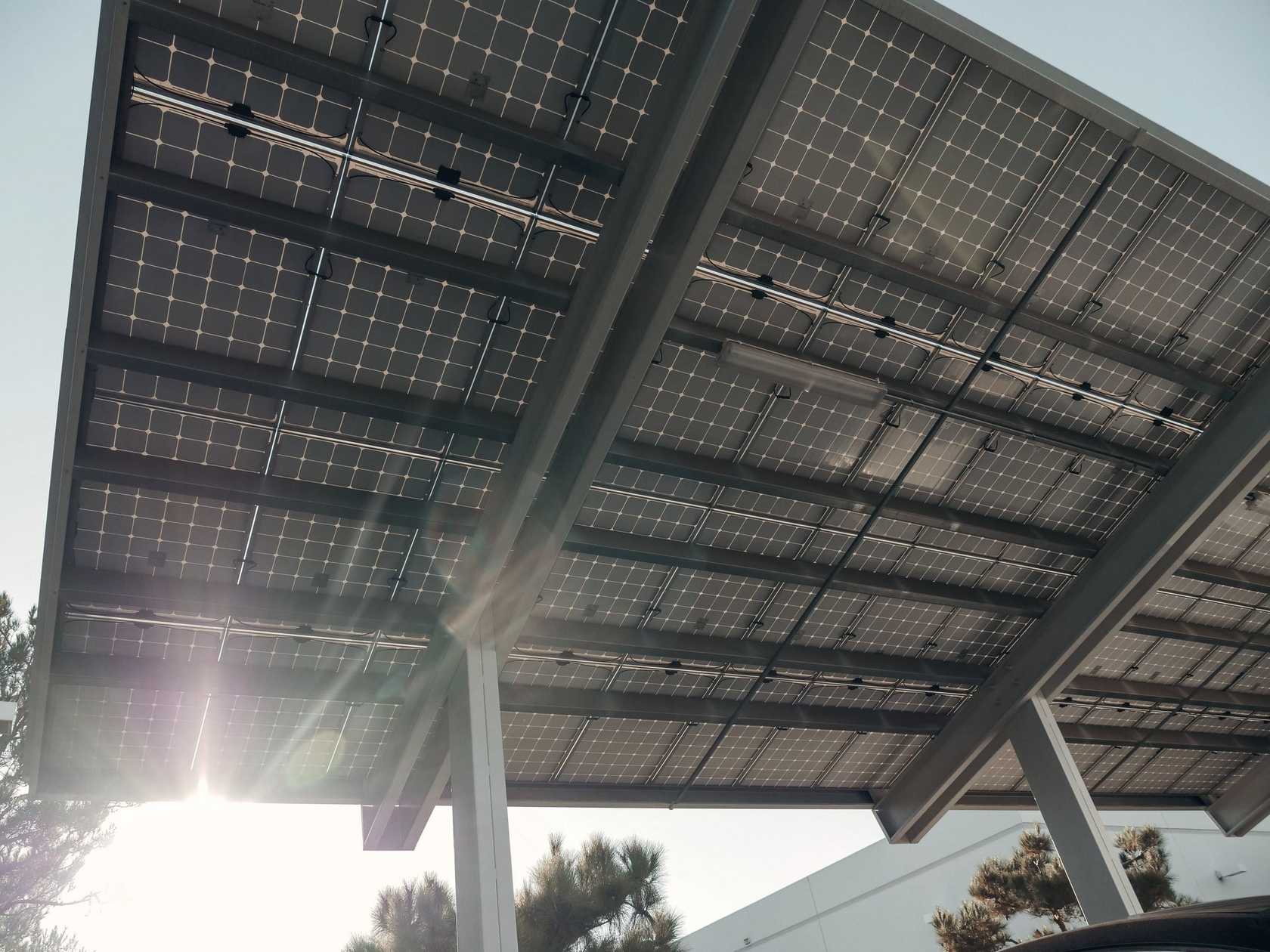 Vue depuis le dessous d'une ombrière photovoltaïque : le soleil passe entre les rangées de panneaux