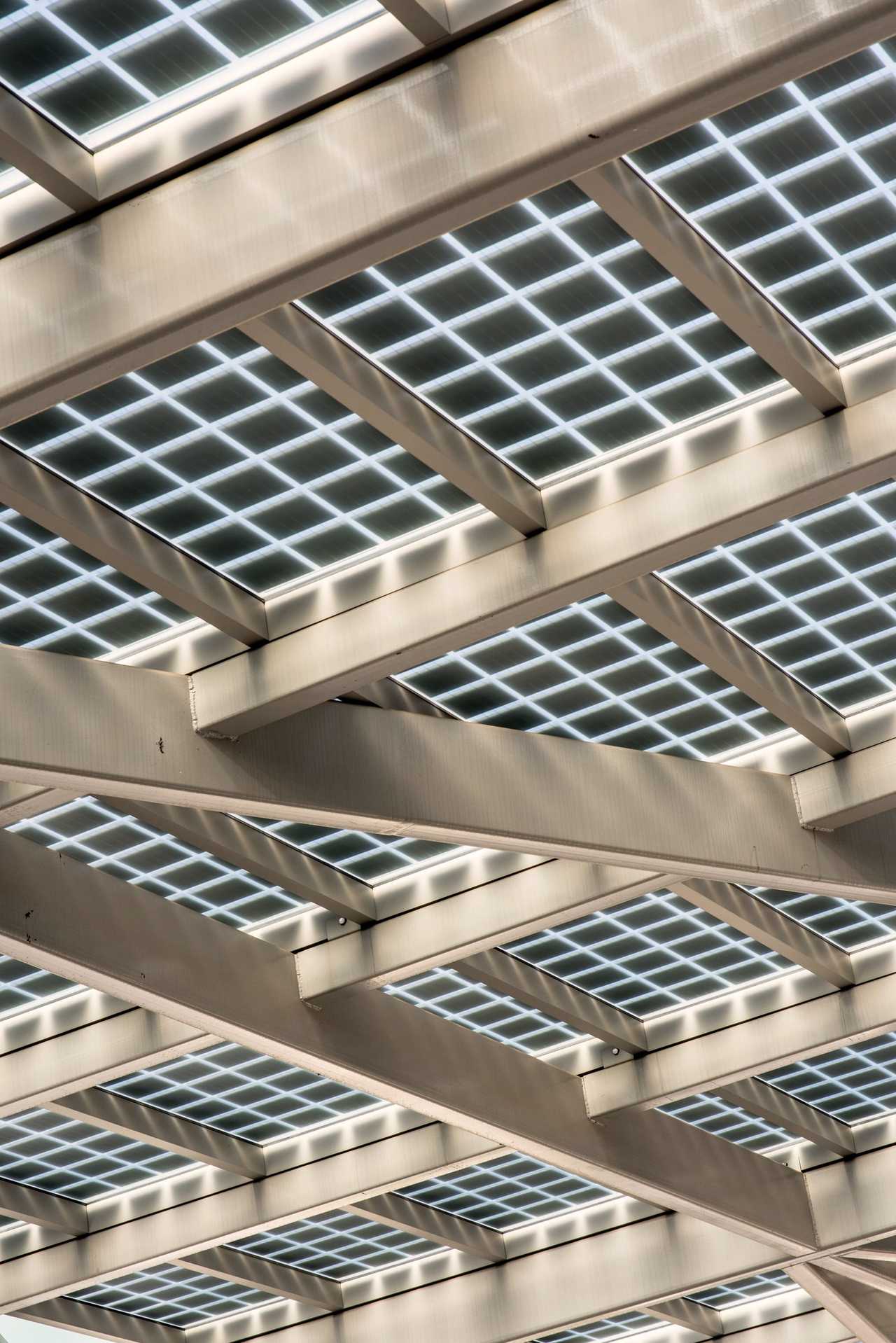 Pergola photovoltaïque vue de dessous : panneaux verriers translucides posés sur des poutres claires